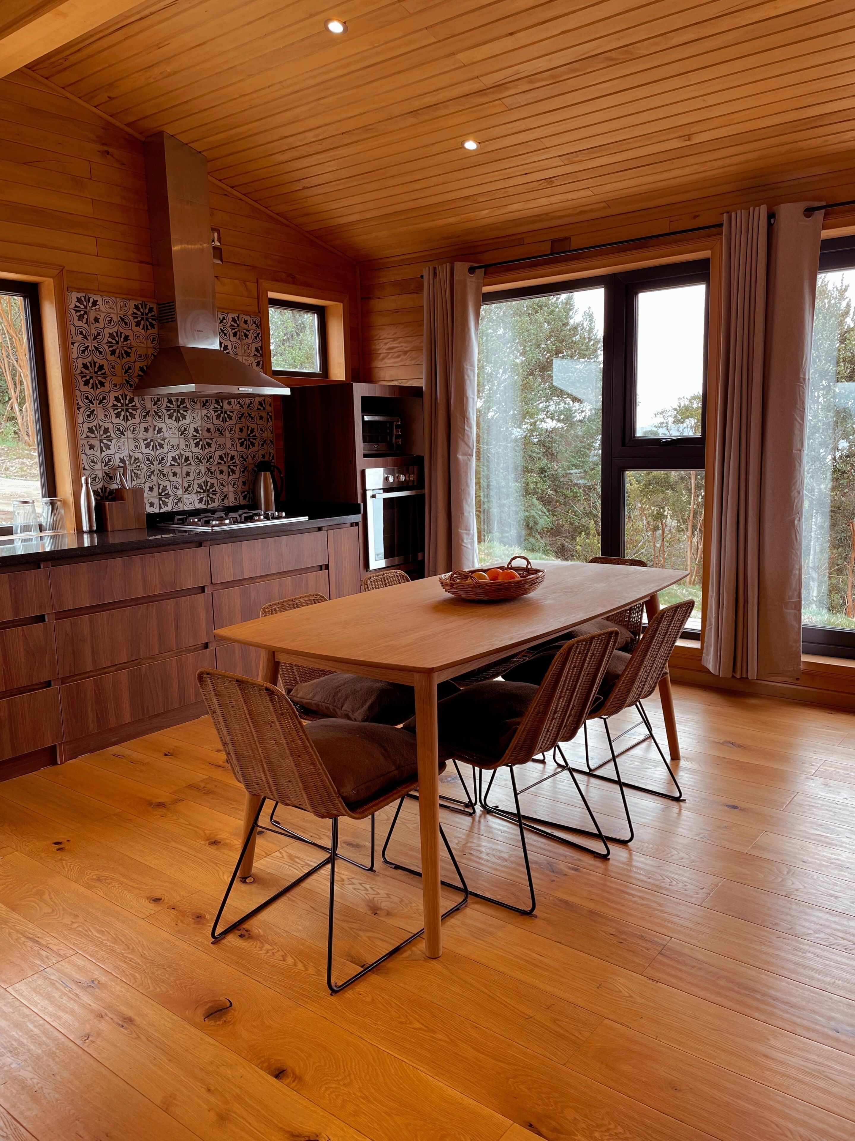 A modern kitchen with wooden cabinets, a large window, and a dining area with a wooden table and chairs.