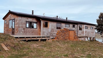 A wooden cabin with a deck, a chimney, and a stack of firewood.