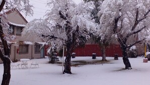 A snow-covered outdoor area with trees, a red building, and outdoor seating. - Cabañas Solitudine (Las Compuertas)