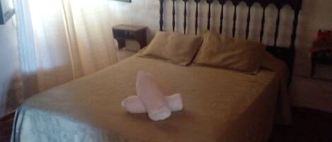 Una cama con cabecera de madera, una mesita de noche y una ventana con cortinas.