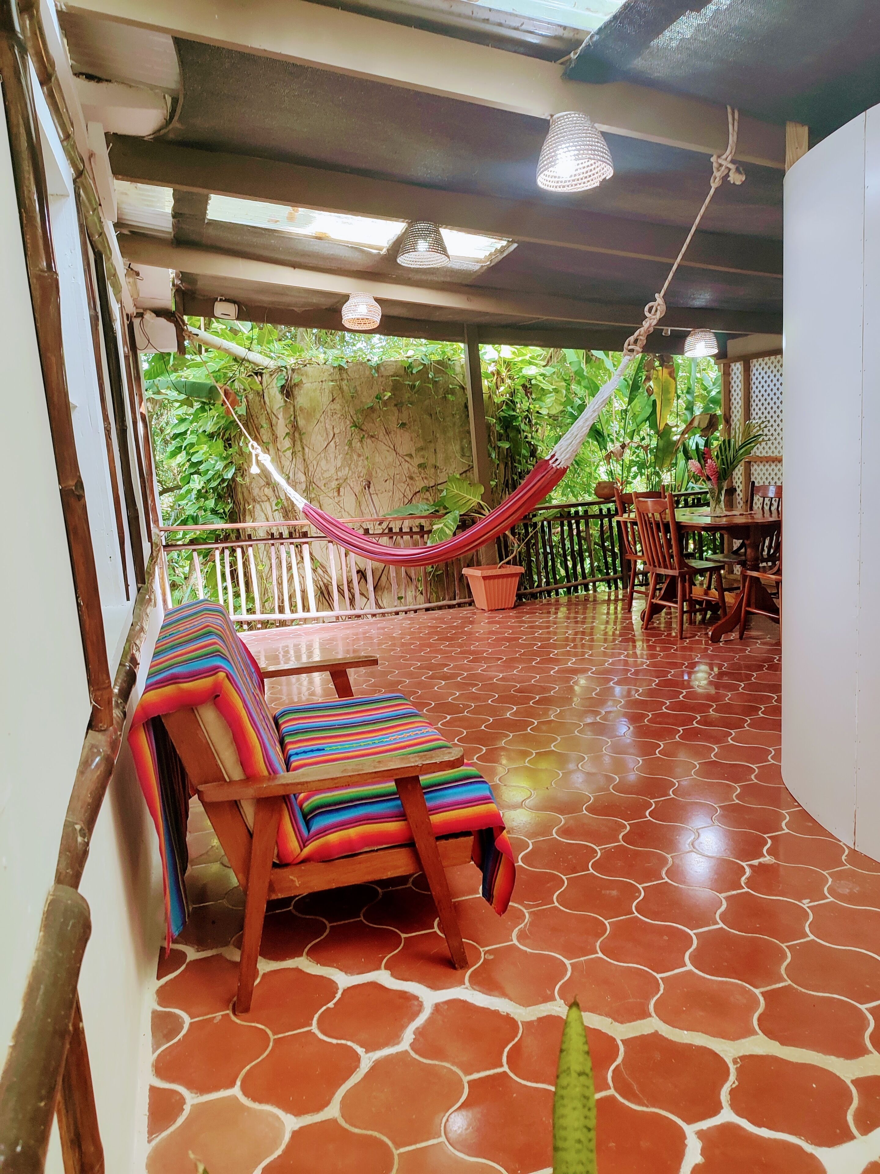 A covered patio area with a hammock, wooden chairs, and a table.
