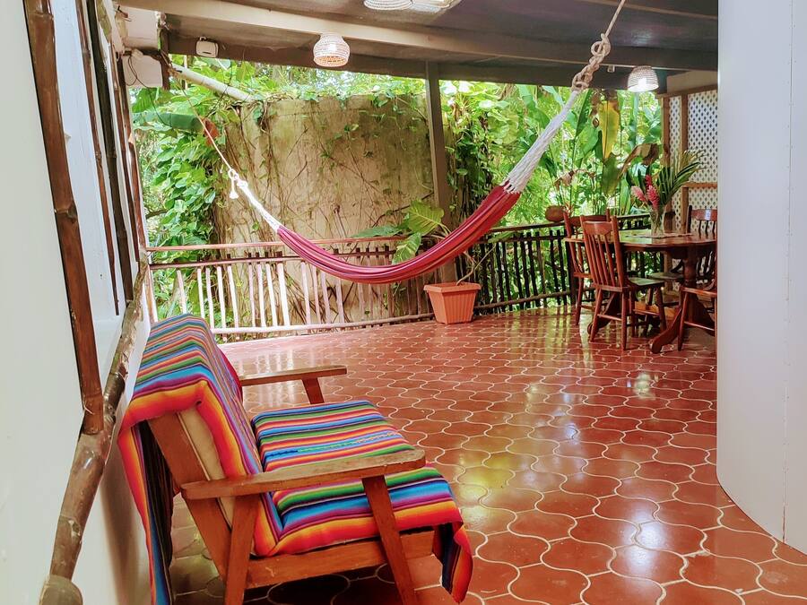 A covered patio area with a hammock, wooden chairs, and a table.