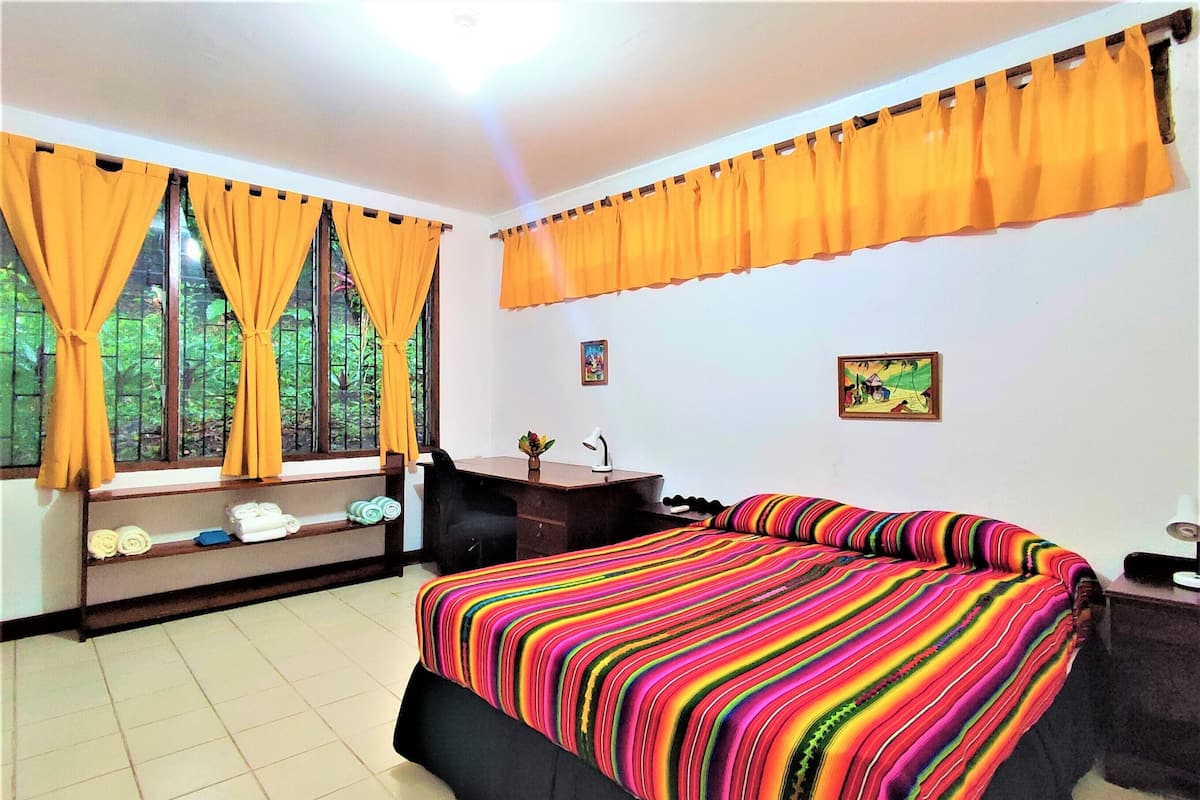 A hotel room with a large bed, a desk, and a window with curtains.