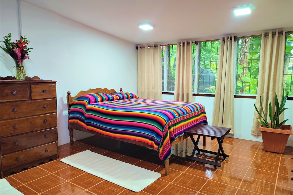 A bedroom with a wooden bed, a dresser, a bench, and a potted plant.
