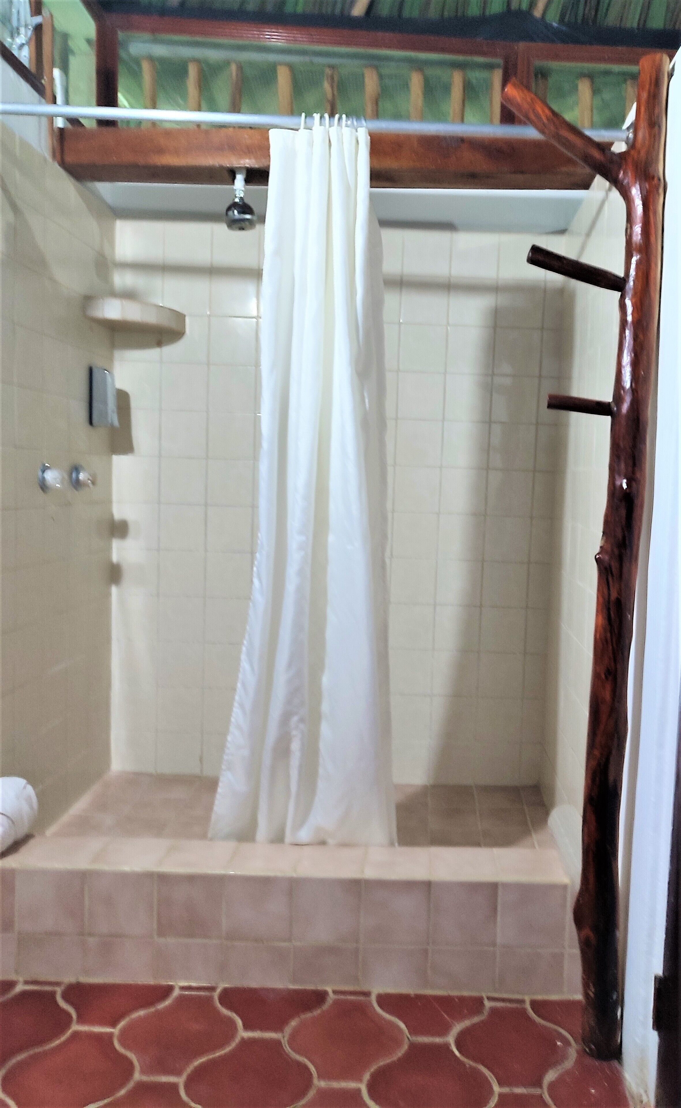 A shower area with a white curtain, tiled walls, and a wooden structure above.