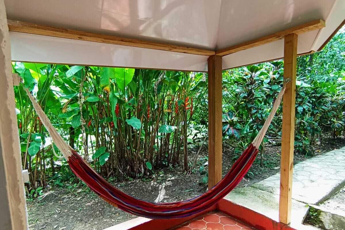 A hammock in a covered outdoor area with a tiled floor and a view of lush greenery.