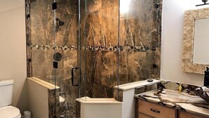Un baño con ducha envuelta en vidrio, salpicadero de mármol y lavabo con encimera de piedra.