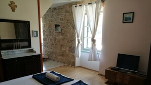 Habitación de hotel con pared de piedra, cama con toalla enrollada, televisor y mueble de madera.