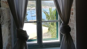 Vista a través de una ventana con cortinas atadas en la parte superior, mostrando un paisaje costero con edificios y barcos.
