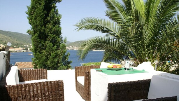 Una terraza con mobiliario de mimbre, una mesa con mantel verde y vistas al mar y las colinas.
