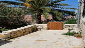 Un patio empedrado con una verja de madera, rodeado de follaje y un muro de piedra.