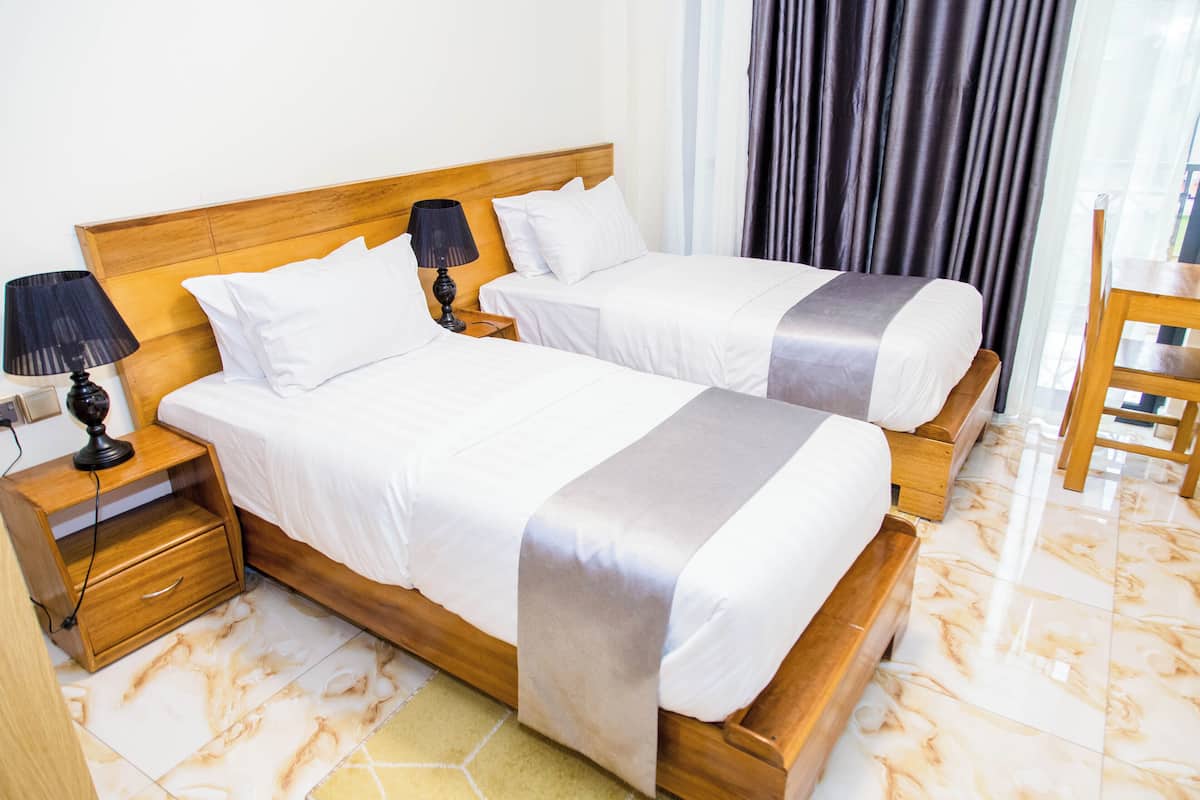 Habitación de hotel con dos camas, cabecero de madera, mesita de noche con lámpara y una silla.