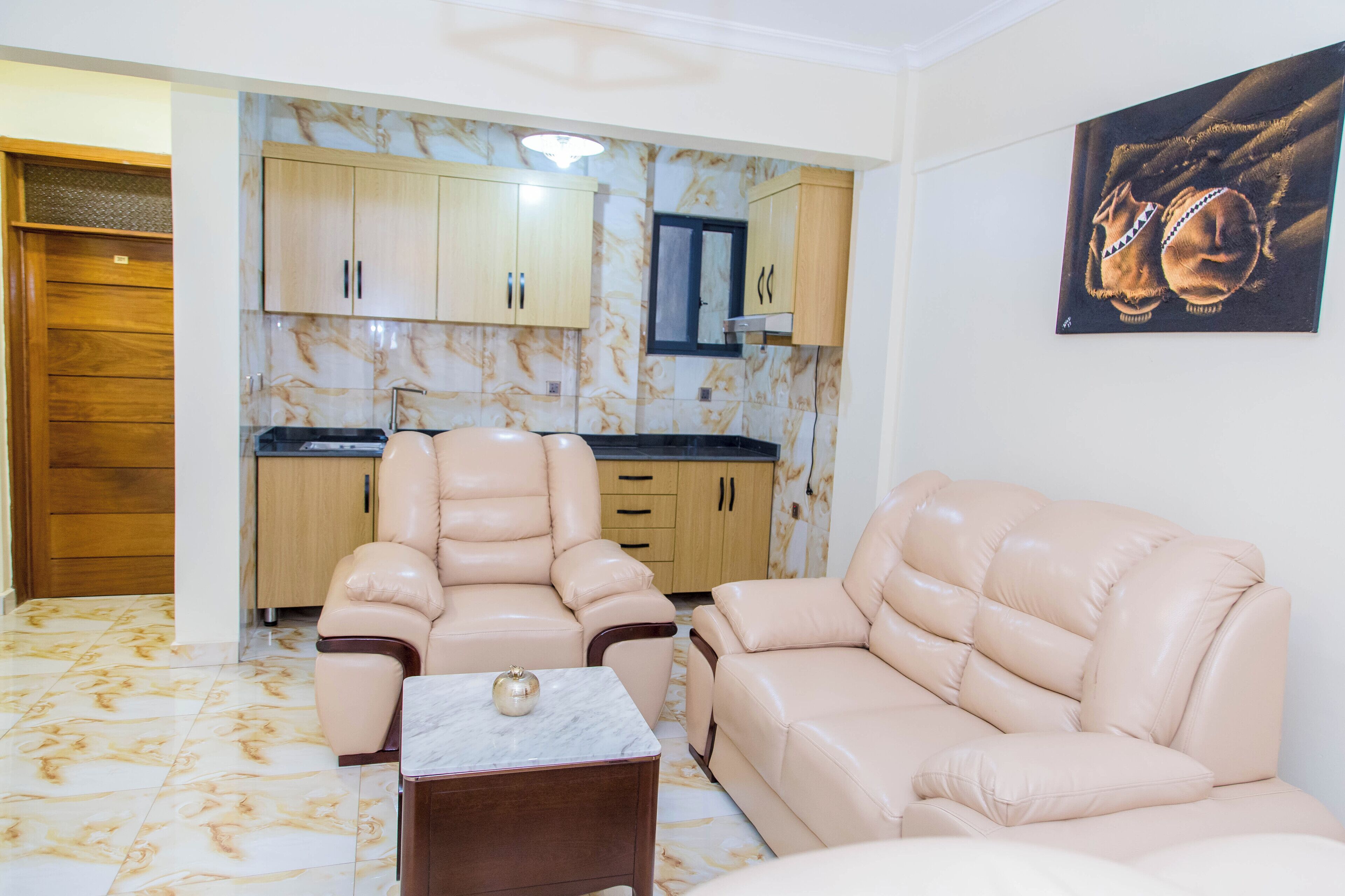 Sala de estar con dos sofás color beige, una mesita y una cocina con armarios de madera y salpicadero de mármol.