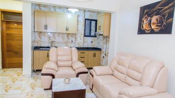 Sala de estar con dos sofás color beige, una mesita y una cocina con armarios de madera y salpicadero de mármol.