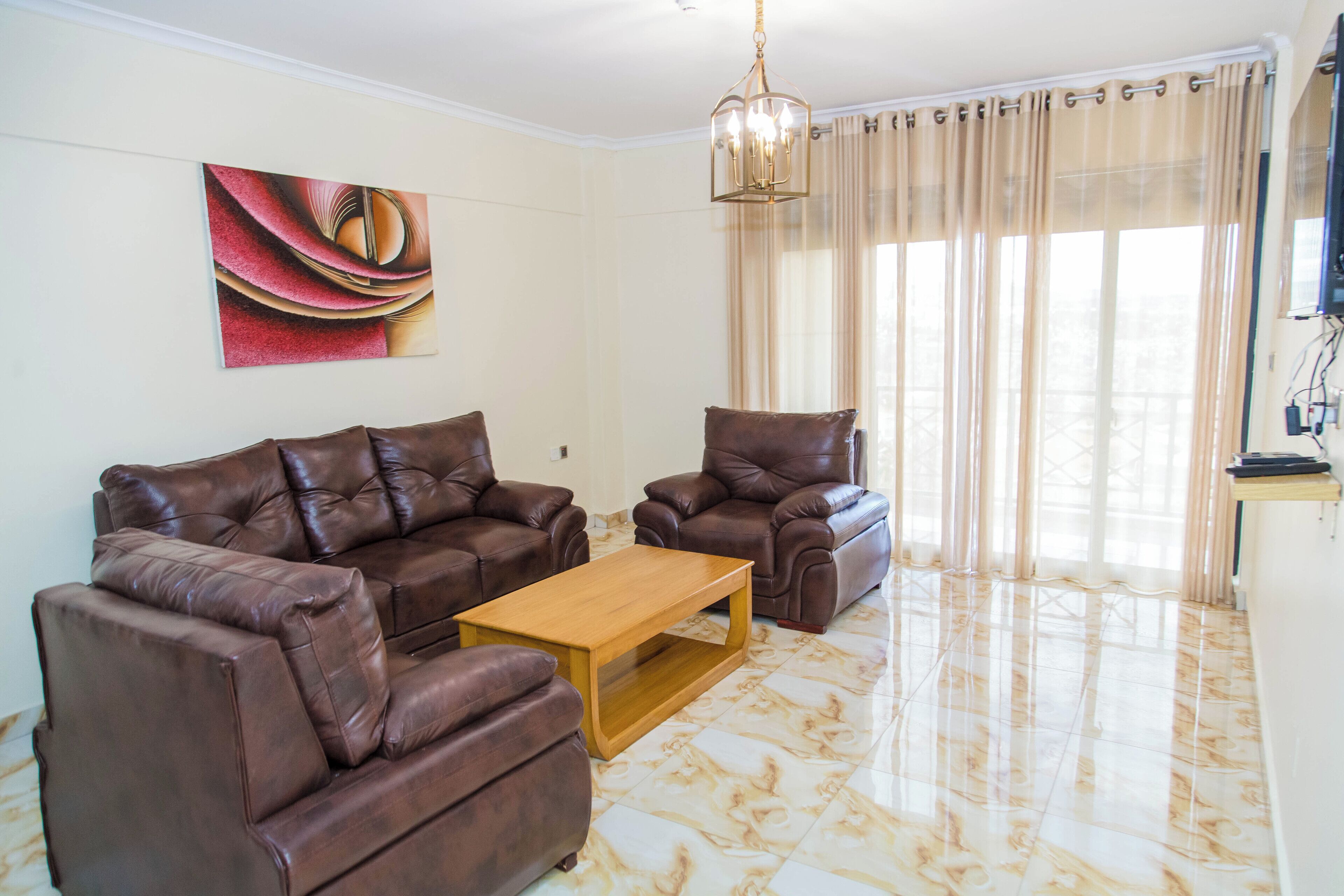 Un soggiorno con un divano in pelle marrone, un tavolino in legno e un'ampia finestra con tende color beige.