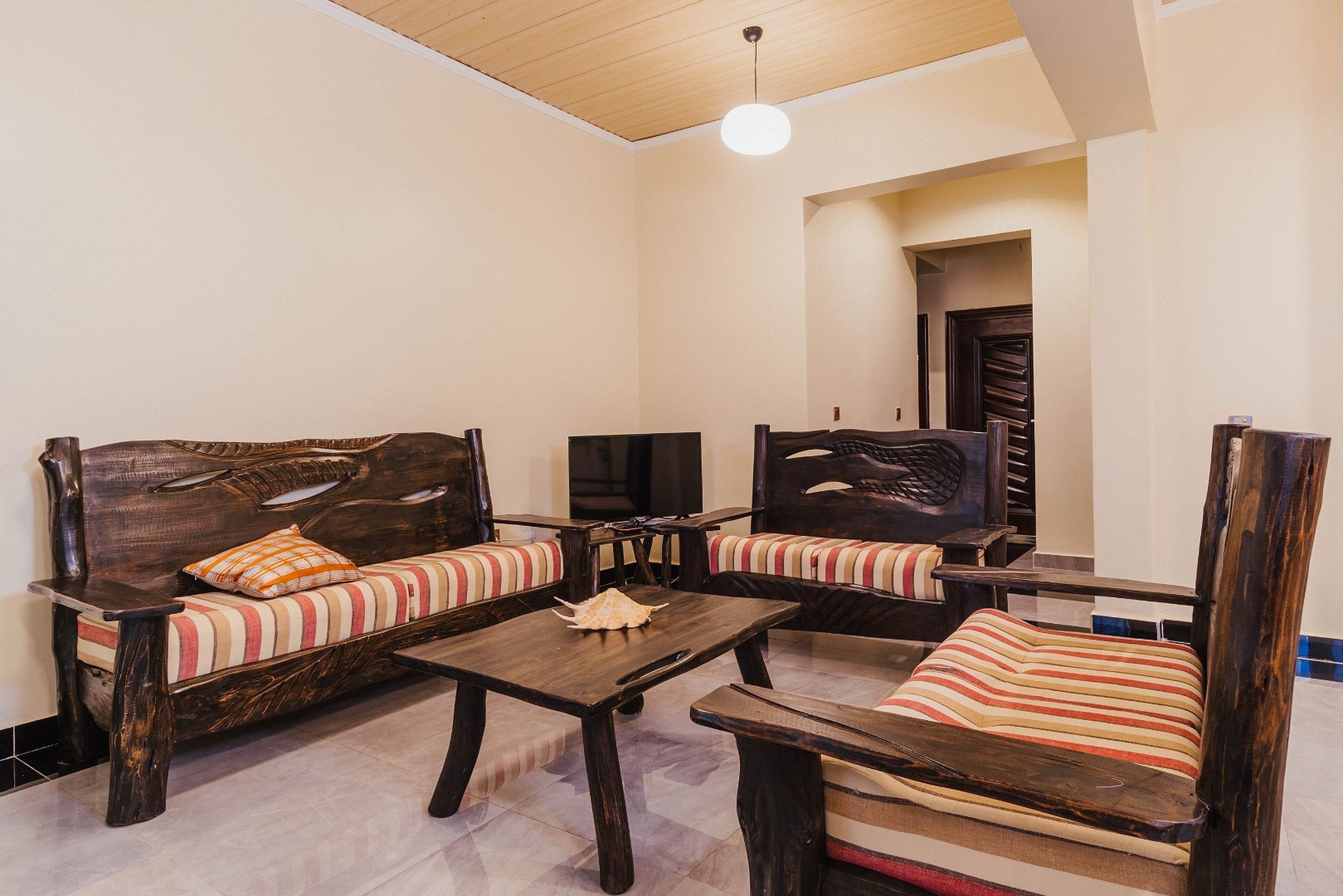 Um quarto com duas sofás de madeira com almofadas listradas, uma mesinha e uma televisão.