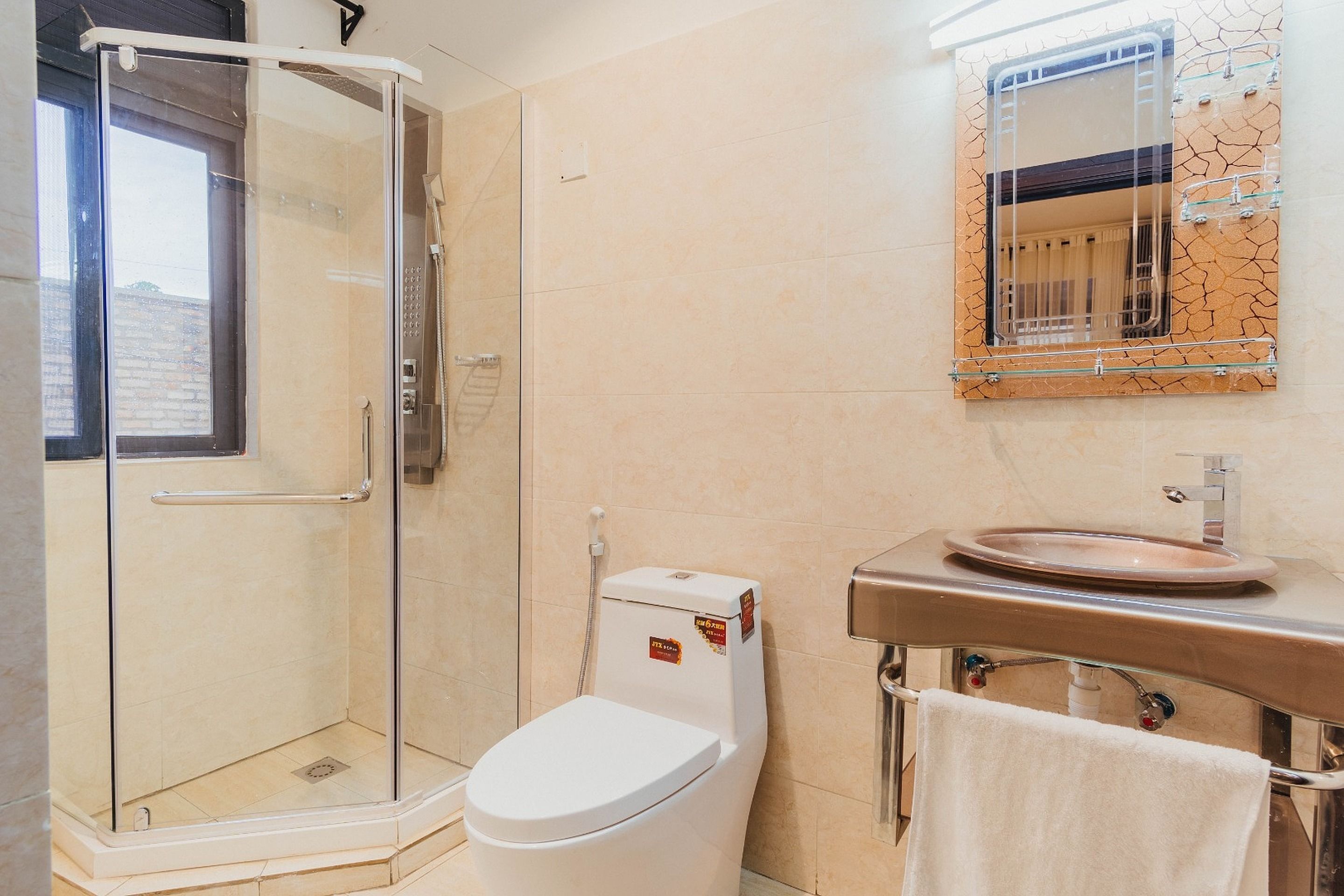 Un baño con cabina de ducha de vidrio, inodoro blanco, lavamanos con espejo y toalla colgada en un perchero.