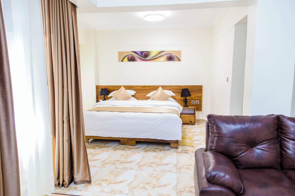 Habitación de hotel con una cama, cabecera de madera, dos lámparas de noche, un sofá de cuero marrón y piso de mármol.