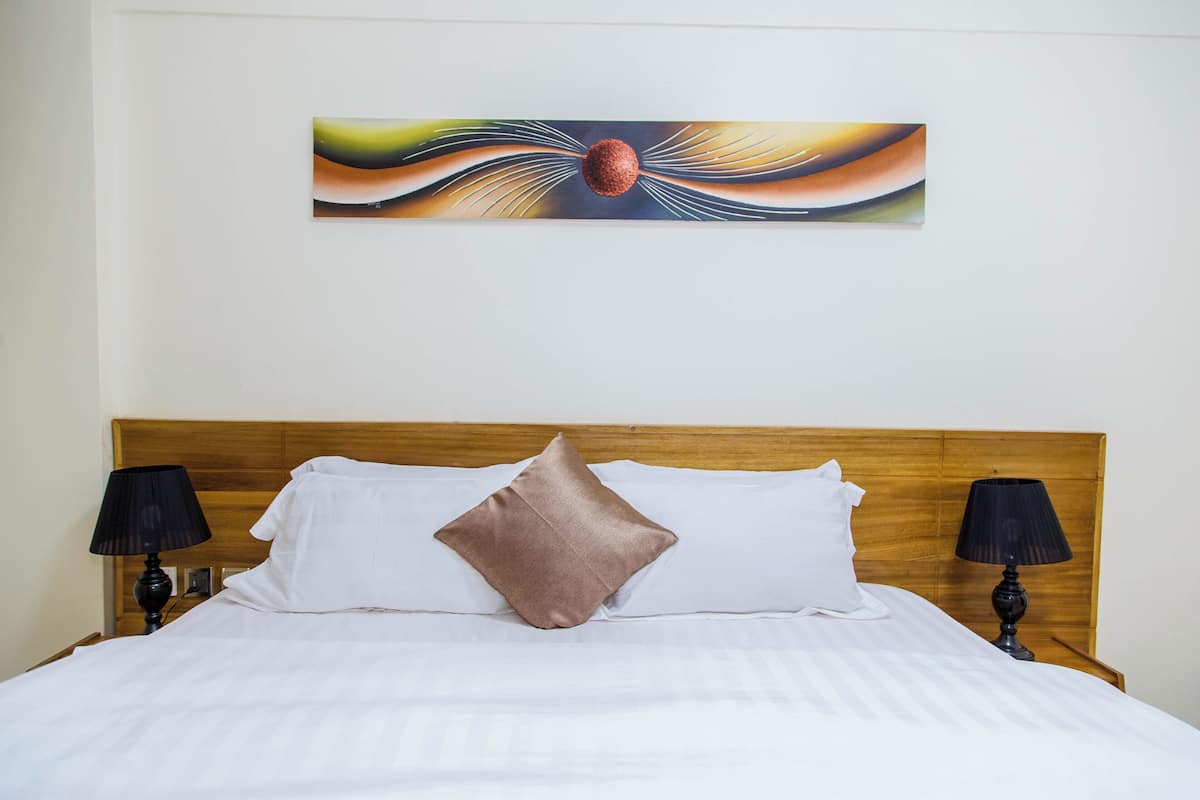 Una cama bien tendida con sábanas blancas y dos almohadas, un cabecero de madera y dos lámparas de noche.