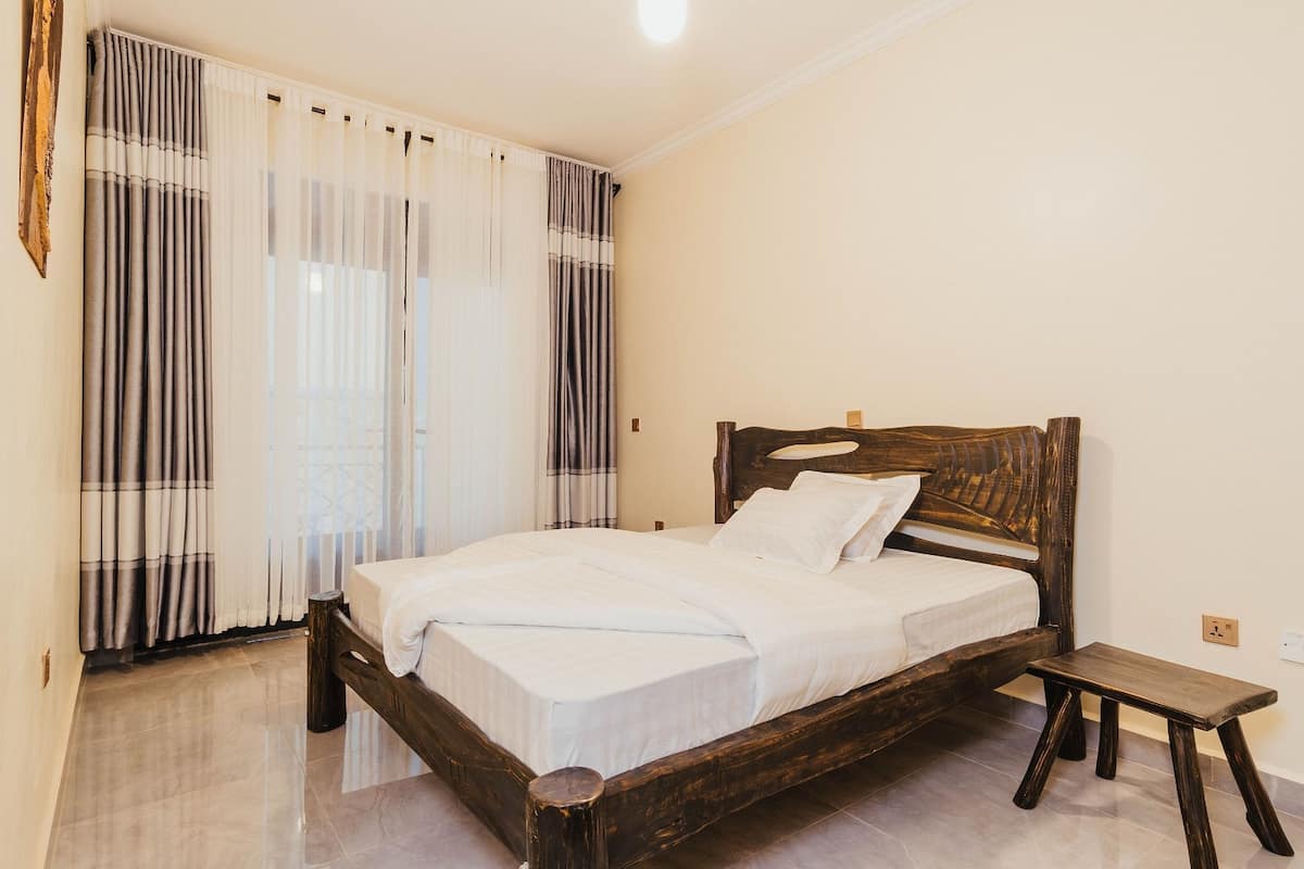 Un dormitorio con una cama de madera, ropa de cama blanca, una mesita de noche de madera y cortinas de encaje.