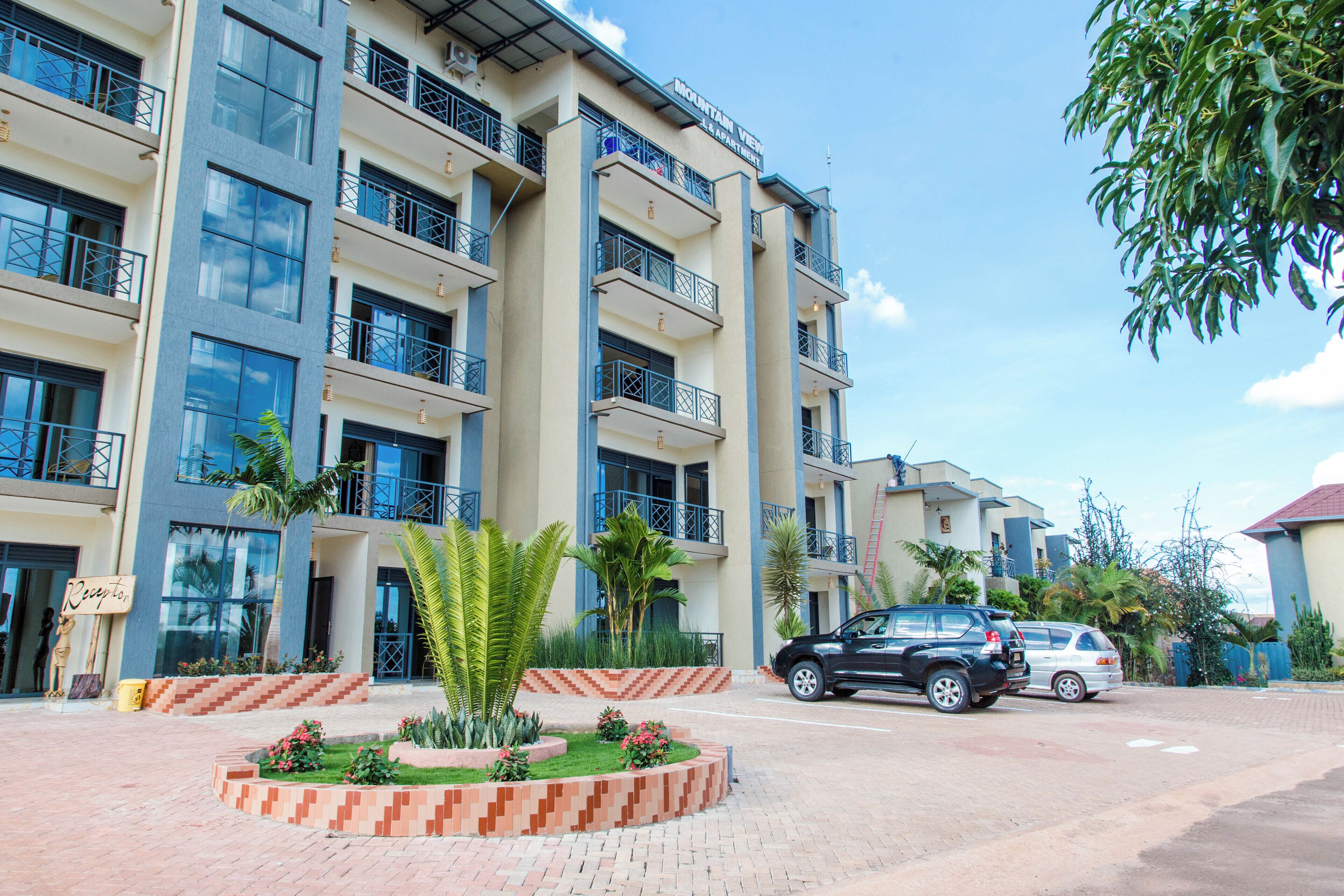 A multi-story hotel with balconies, a landscaped garden, and parked cars.