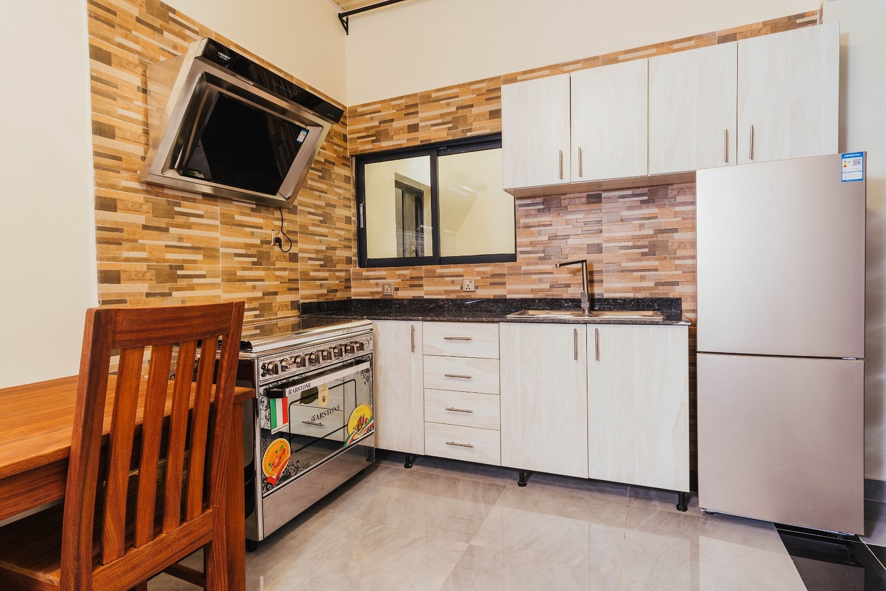 Una cocina con microondas, horno y refrigerador, armarios de madera y una ventana.