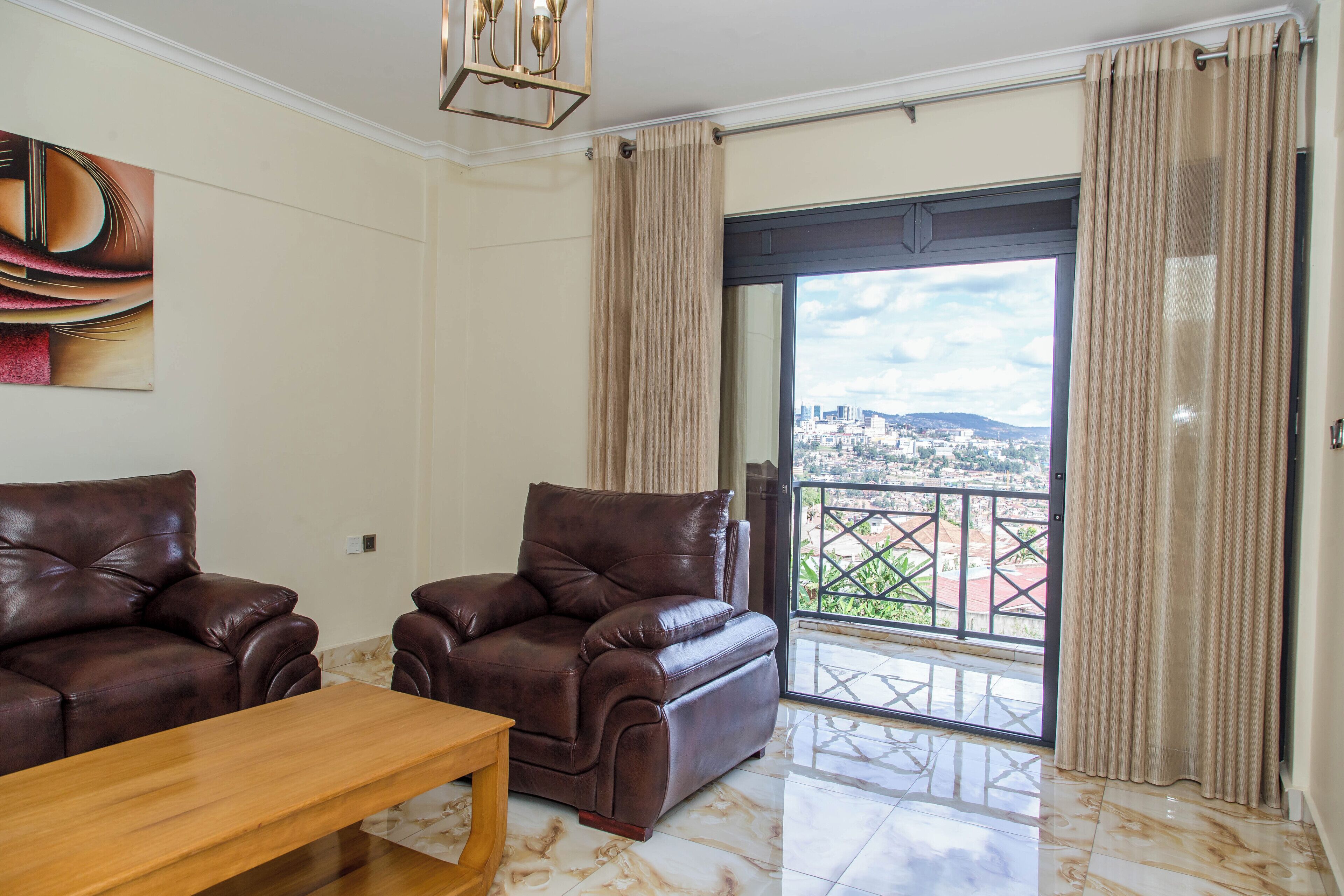Una sala de estar con dos sofás de cuero, una mesa de centro de madera y un amplio ventanal corredero que da a un balcón con vistas a la ciudad.