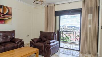 Una sala de estar con dos sofás de cuero, una mesa de centro de madera y un amplio ventanal corredero que da a un balcón con vistas a la ciudad.