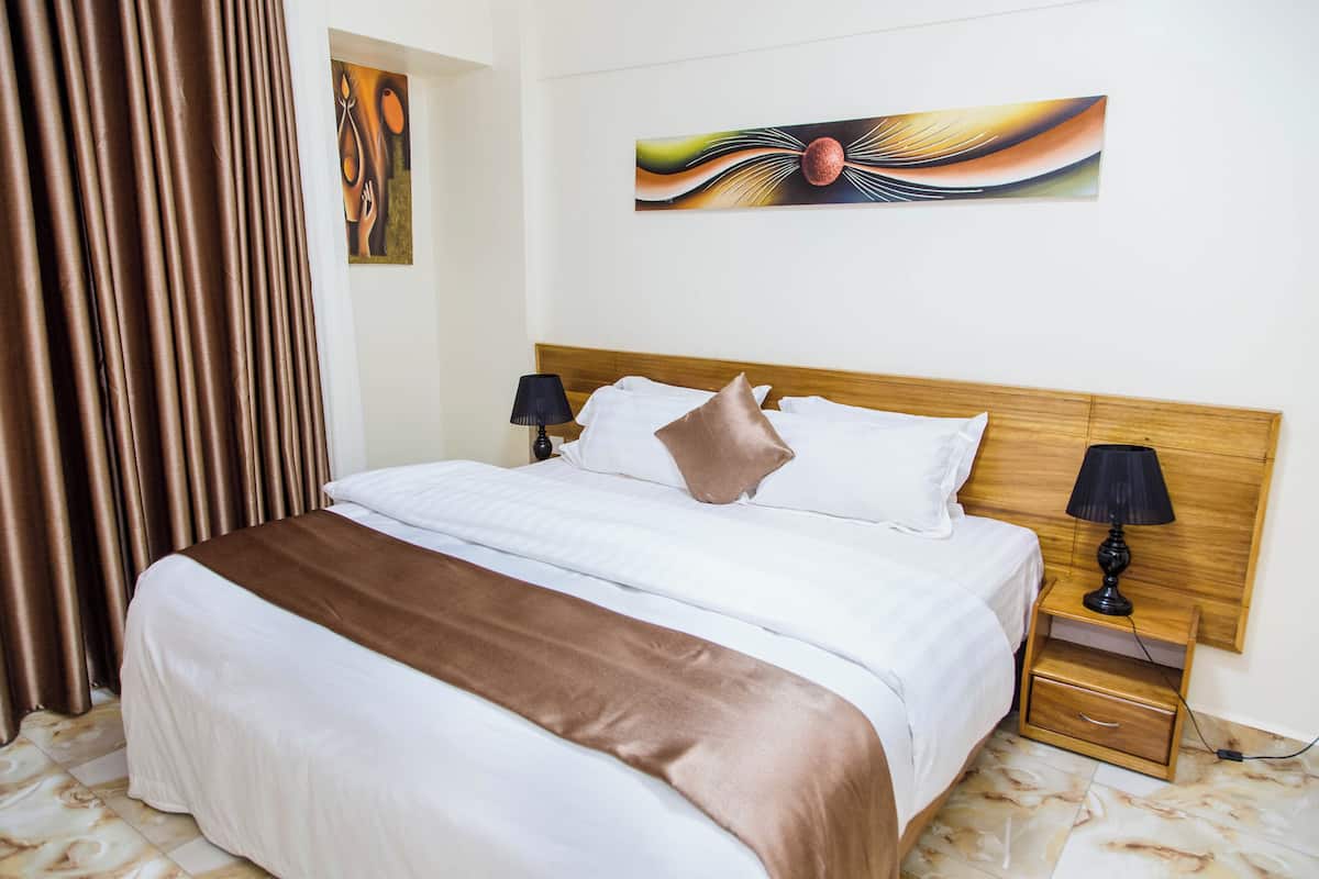 Una cama bien hecha con un plaid marrón, un cabecero de madera, dos mesitas de noche con lámparas y un cuadro en la pared.