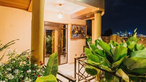 A well-lit entrance with large columns, a framed painting, and lush greenery.