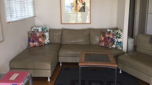 Ein Wohnzimmer mit einem beigefarbenen Ecksofa, einem kleinen Couchtisch und bunten, gemusterten Kissen.
