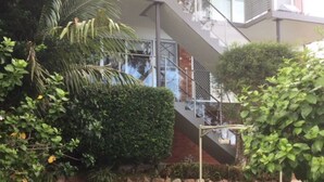 Ein modernes Gebäude mit einer Treppe, die zu einer oberen Ebene führt, umgeben von gepflegter Bepflanzung und einer kleinen Rasenfläche.