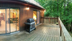 Une cabane en bois dotée d’une terrasse, d’un barbecue et d’une porte vitrée donnant sur un espace intérieur comprenant un coin repas.