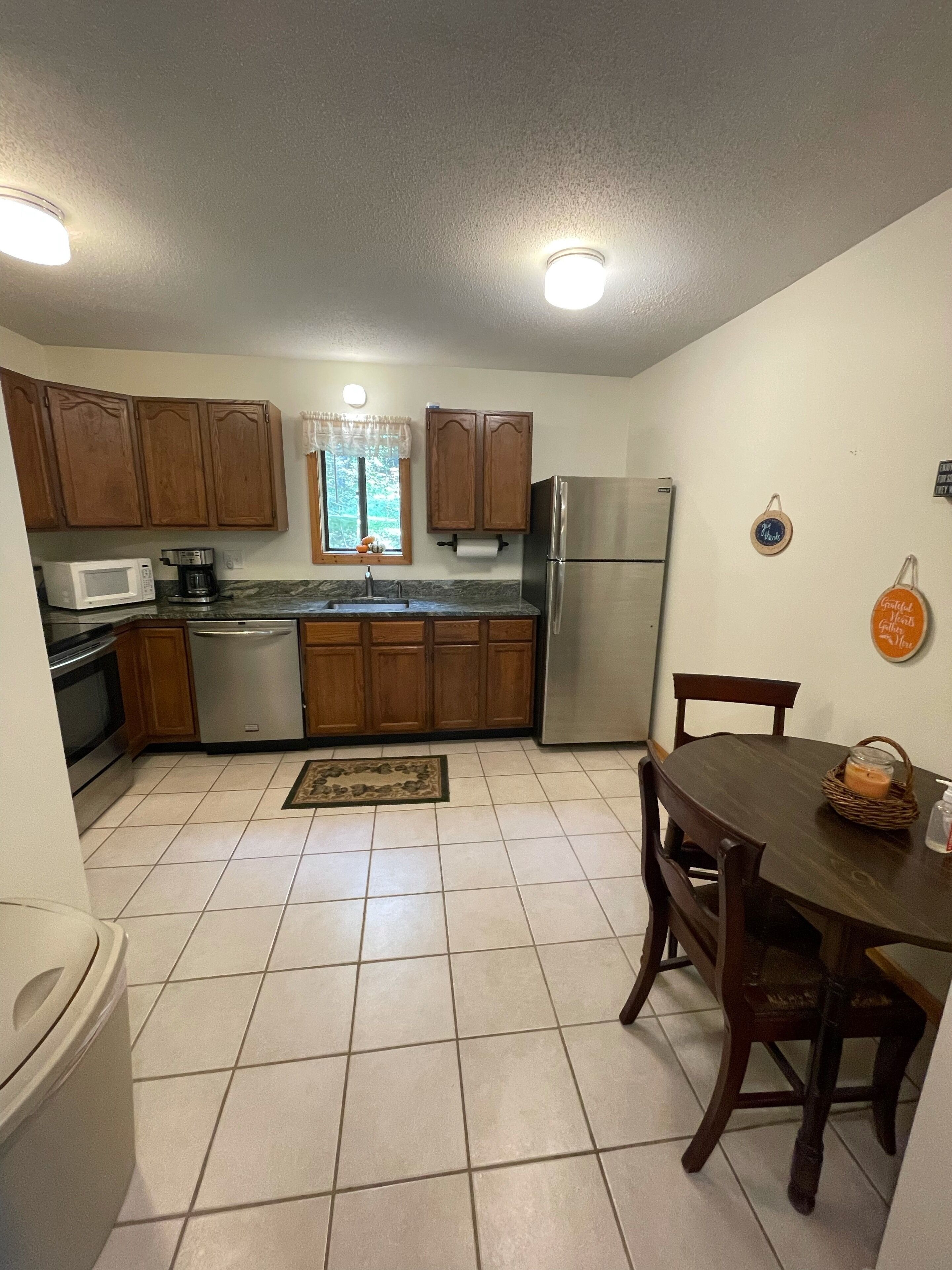 A compact kitchen with wooden cabinets, a stainless steel refrigerator, a microwave, and a dining table with chairs.