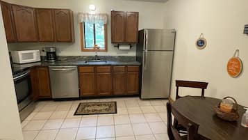A compact kitchen with wooden cabinets, a stainless steel refrigerator, a microwave, and a dining table with chairs.