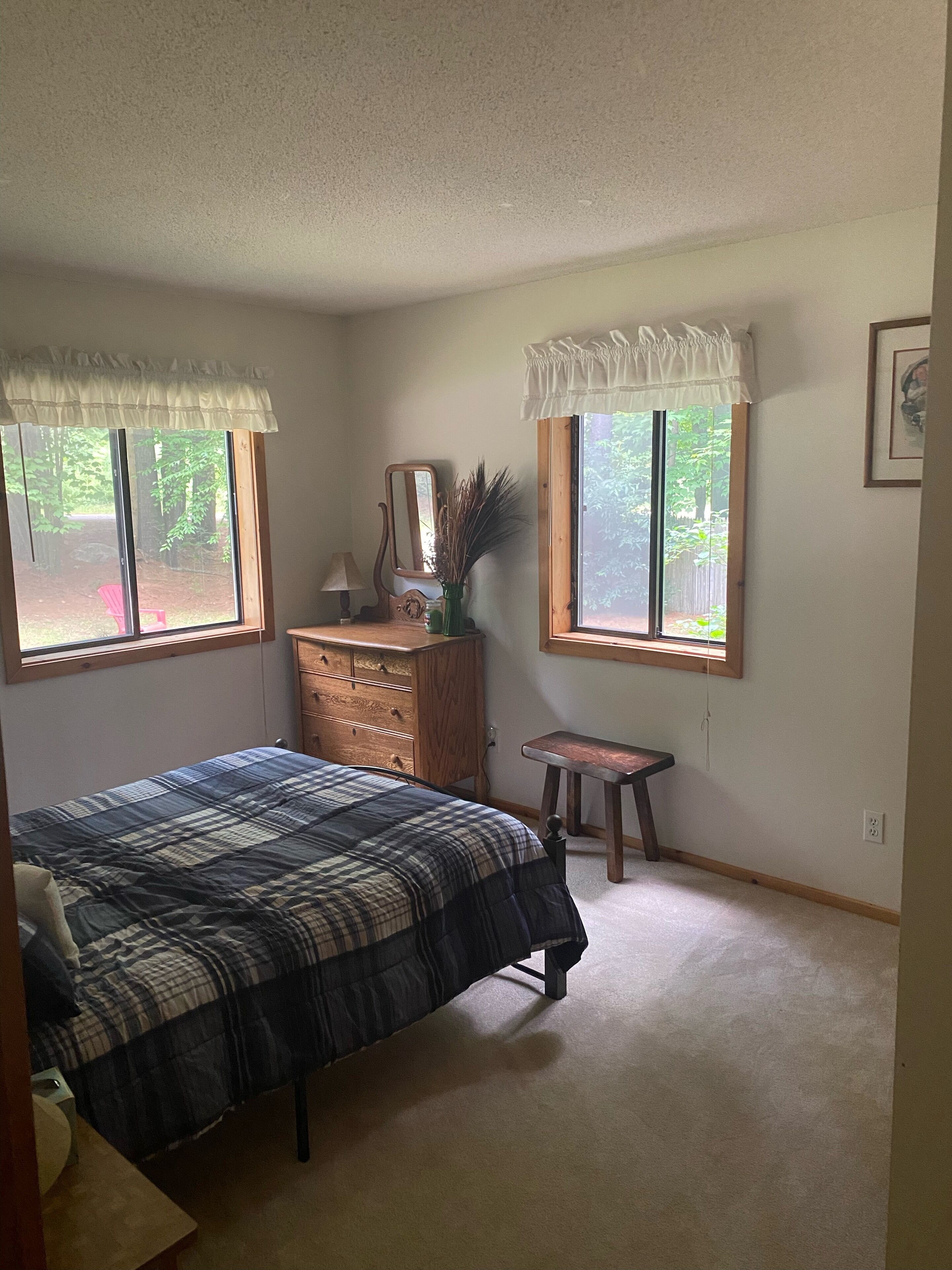 A bedroom with a bed, dresser, vanity, and two windows with curtains.
