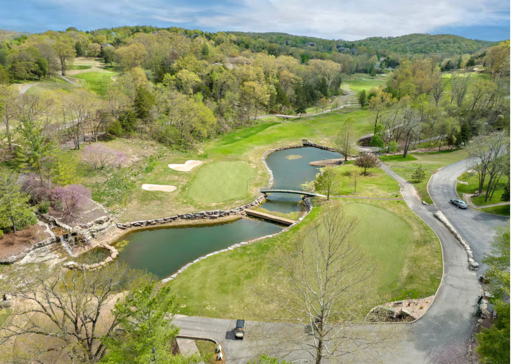 Un campo de golf con un estanque, un puente y un camino sinuoso.