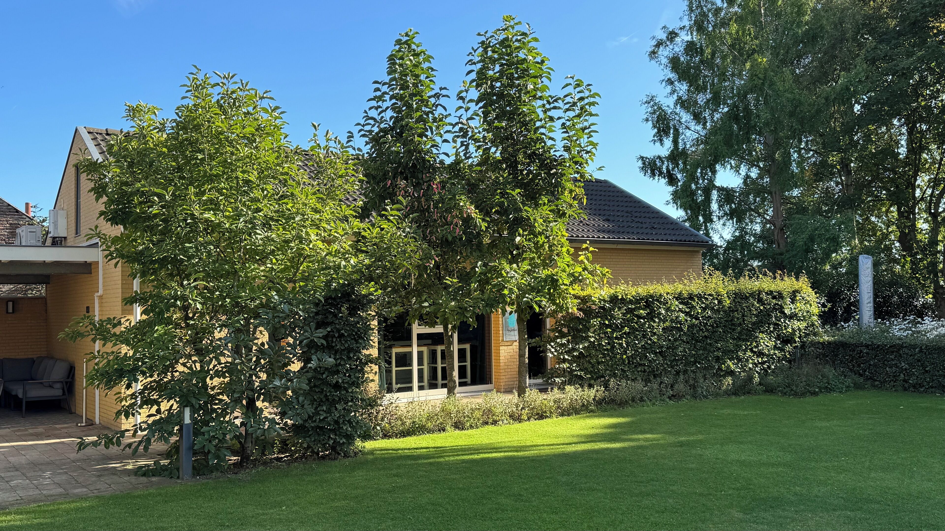 A residential building with a well-maintained lawn, a hedge, and a clear blue sky.