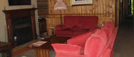 A living room with a fireplace, a red sofa, a wooden wall, and a clock.