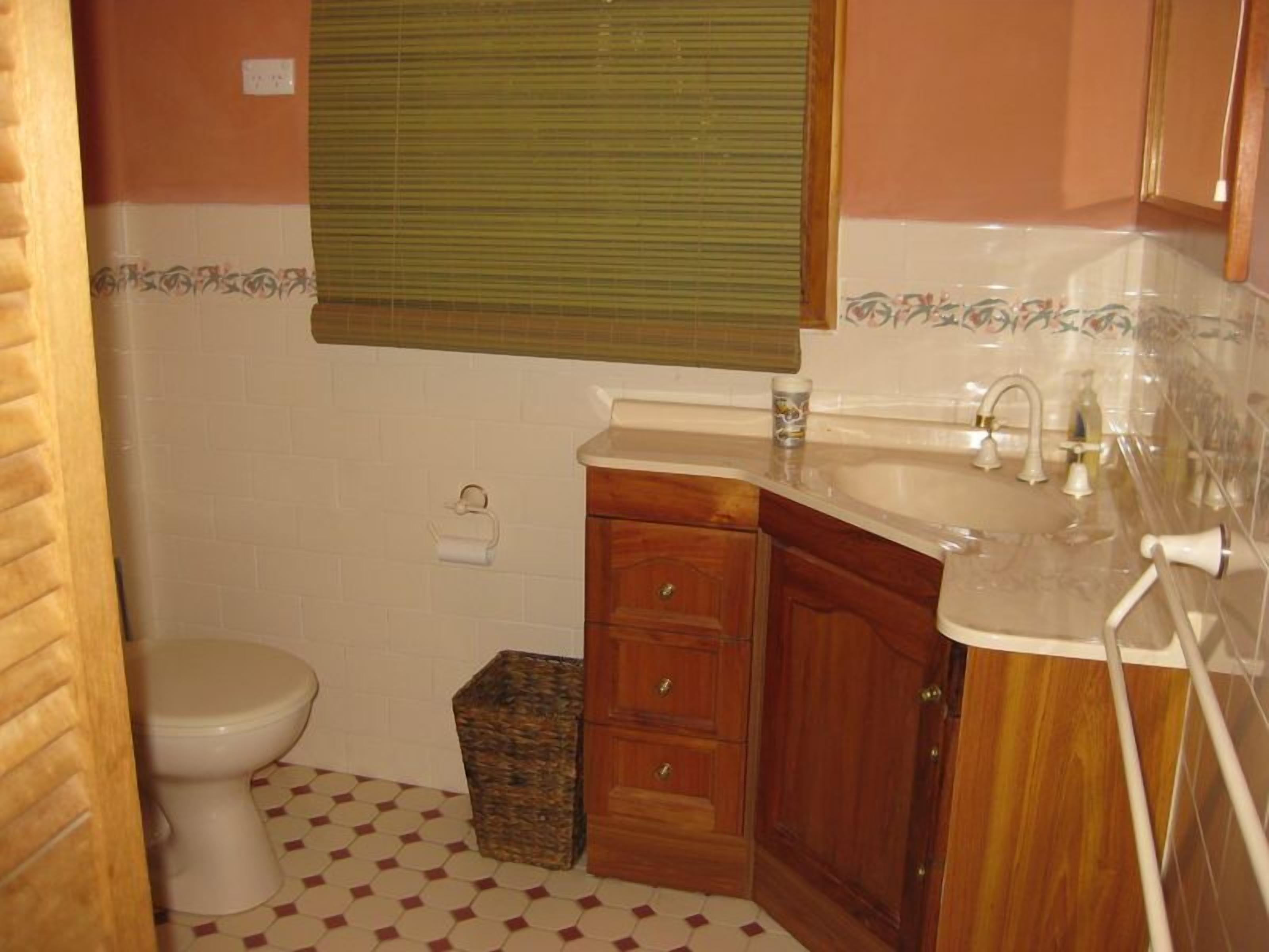 Un baño con inodoro, lavamanos, espejo y un mueble de madera.