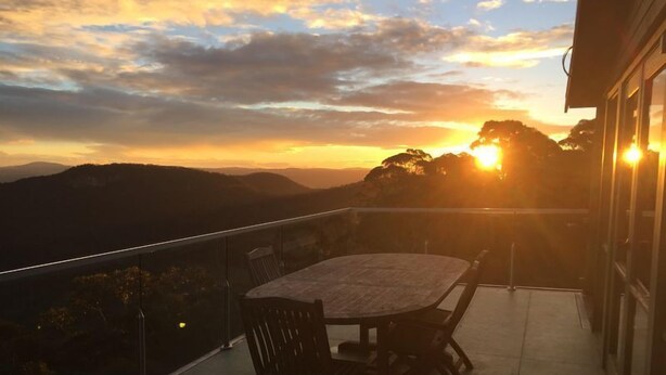 A balcony with a table and chairs, overlooking a mountainous landscape during sunset. - Graceland Mount Victoria (Mount Victoria)