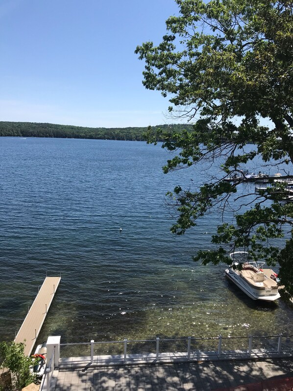 A dock extending into a calm lake with a boat moored nearby, surrounded by trees and a clear sky. - Waterfront Lake Winnipesaukee Luxury Family House with Private Water-Dock+ more (Meredith)