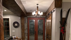 Un corridoio con pavimento a spina di pesce, una panca in legno, una sveglia a muro e una porta doppia con vetri smerigliati.