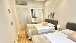 A hotel room with two beds, a wooden floor, a white door, and a mirror. - Spacious 2-bedroom apartment on Paulista Avenue. (São Paulo)