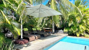 A poolside area with lounge chairs and an umbrella, surrounded by palm trees. - Beach house with 4 suites and a pool. Comfort and privacy just steps from the sea. (Camaçari)
