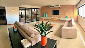 A modern lobby with a sofa, a coffee table, and a potted plant. There is a staircase leading to an upper floor, and a flat-screen TV mounted on the wall. - Vacation - edf. Port Ville III apt 1007 on the top floor with pool panoramic view (Jatiúca)