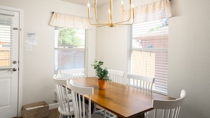 Un coin repas avec une table en bois, des chaises blanches, une plante en pot et un lustre.