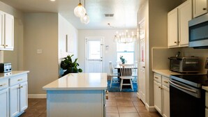 Une cuisine moderne avec des meubles blancs, un îlot central et un coin repas agrémenté d’un tapis bleu.