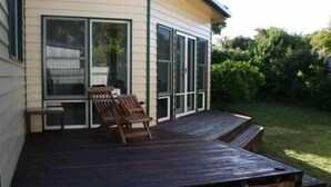 A wooden deck with two chairs, a small table, and a covered area with a glass door leading to a screened porch. - Fitzgerald Cape Paterson (Cape Paterson)
