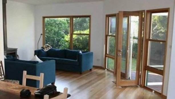 A spacious room with a blue sofa, a dining table with chairs, and large windows offering a view of greenery. - Fitzgerald Cape Paterson (Cape Paterson)